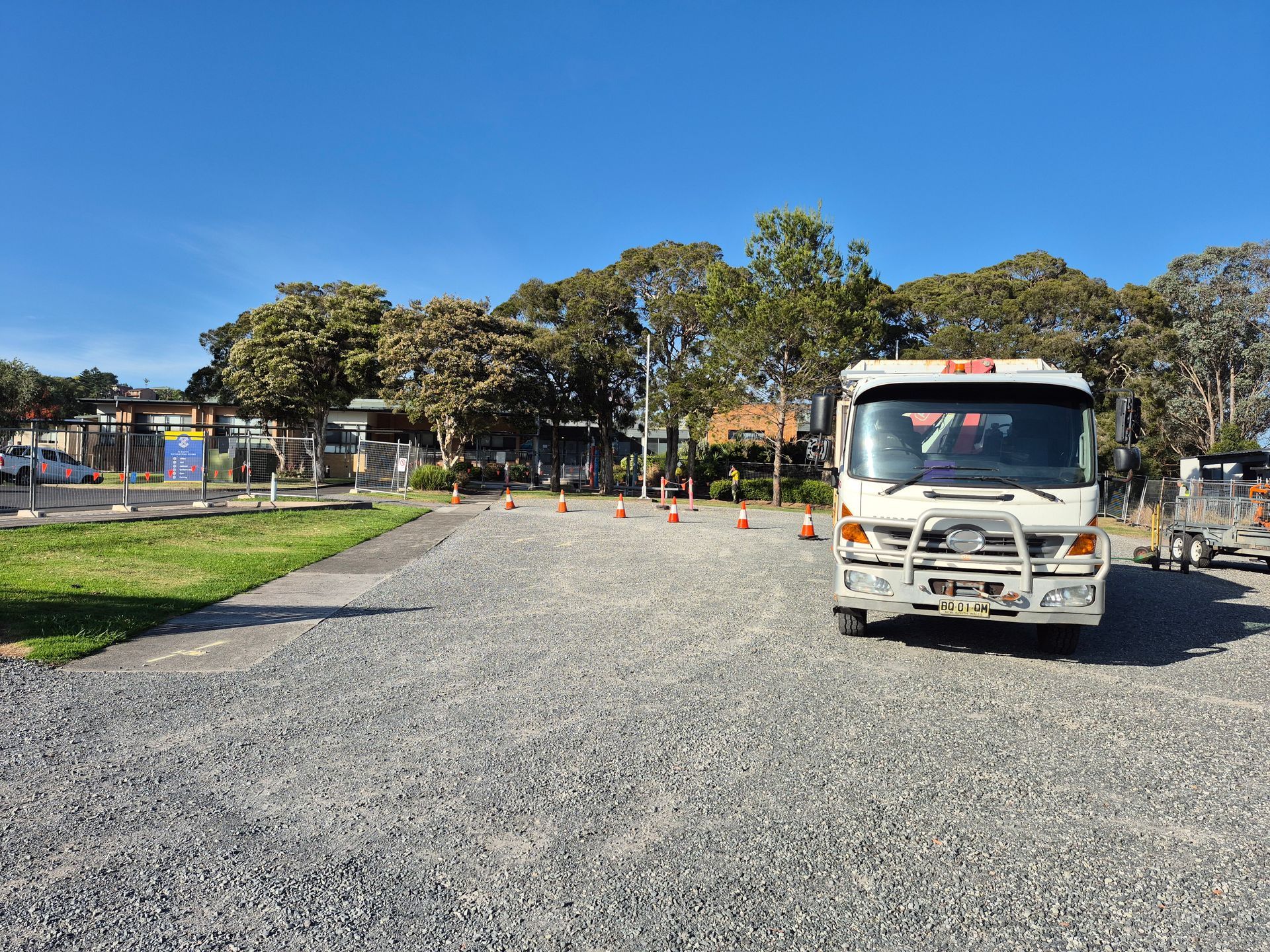 White truck parked on gravel, orange cones, blue sky, trees, and a building.