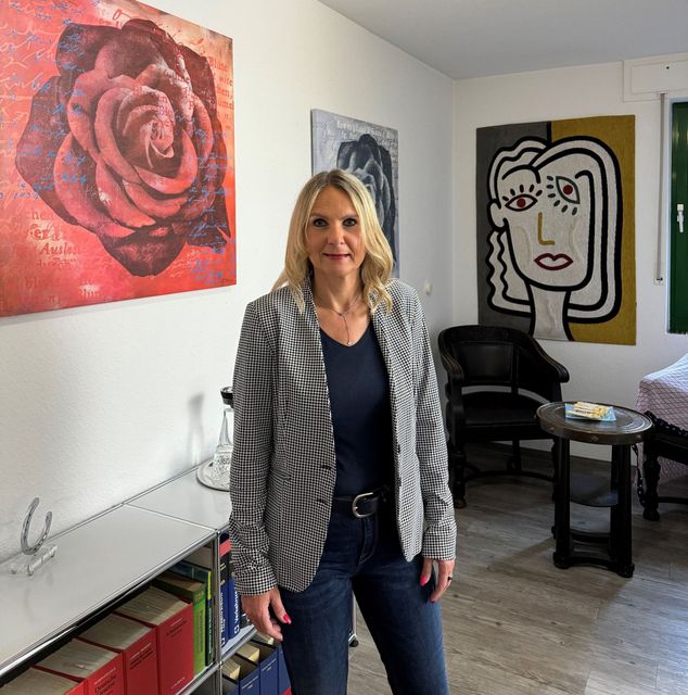 A woman is standing in a living room with a painting of a rose on the wall behind her