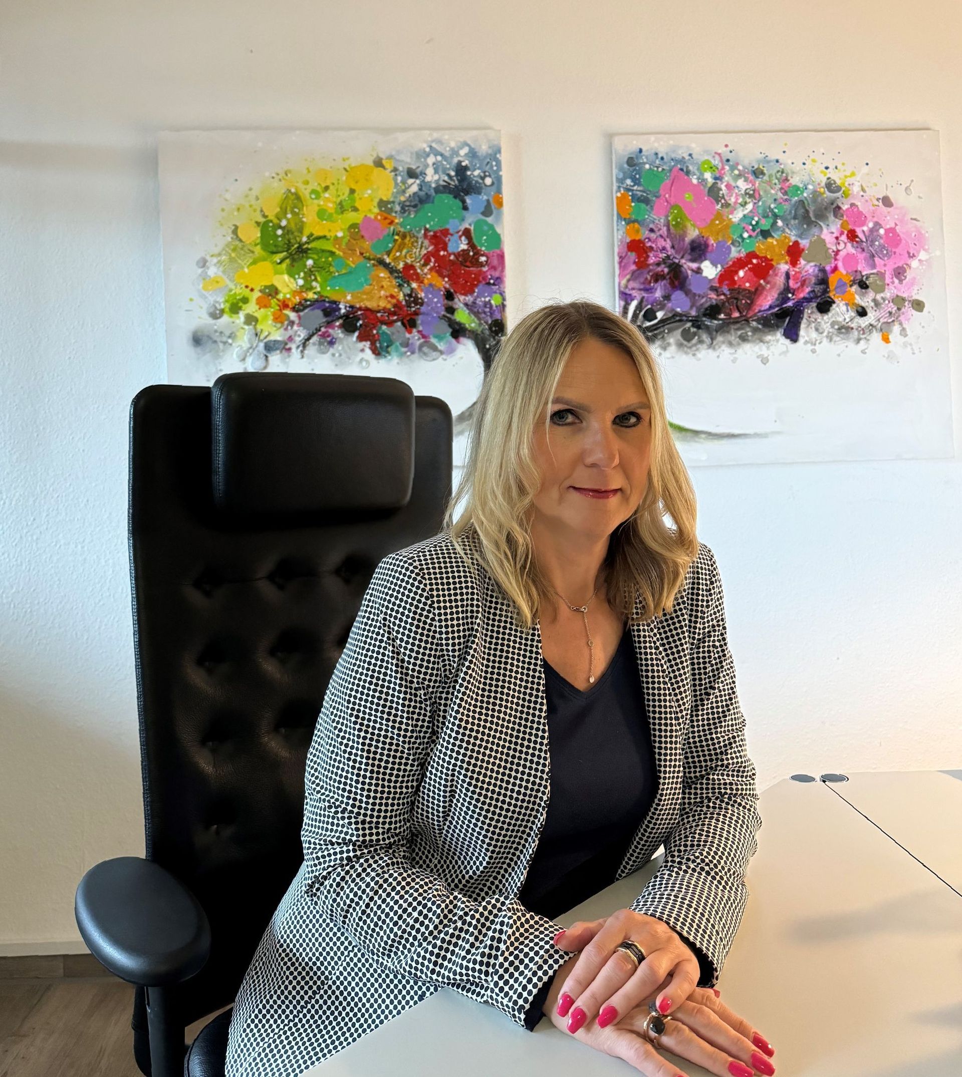 A woman is sitting at a desk with two paintings on the wall behind her