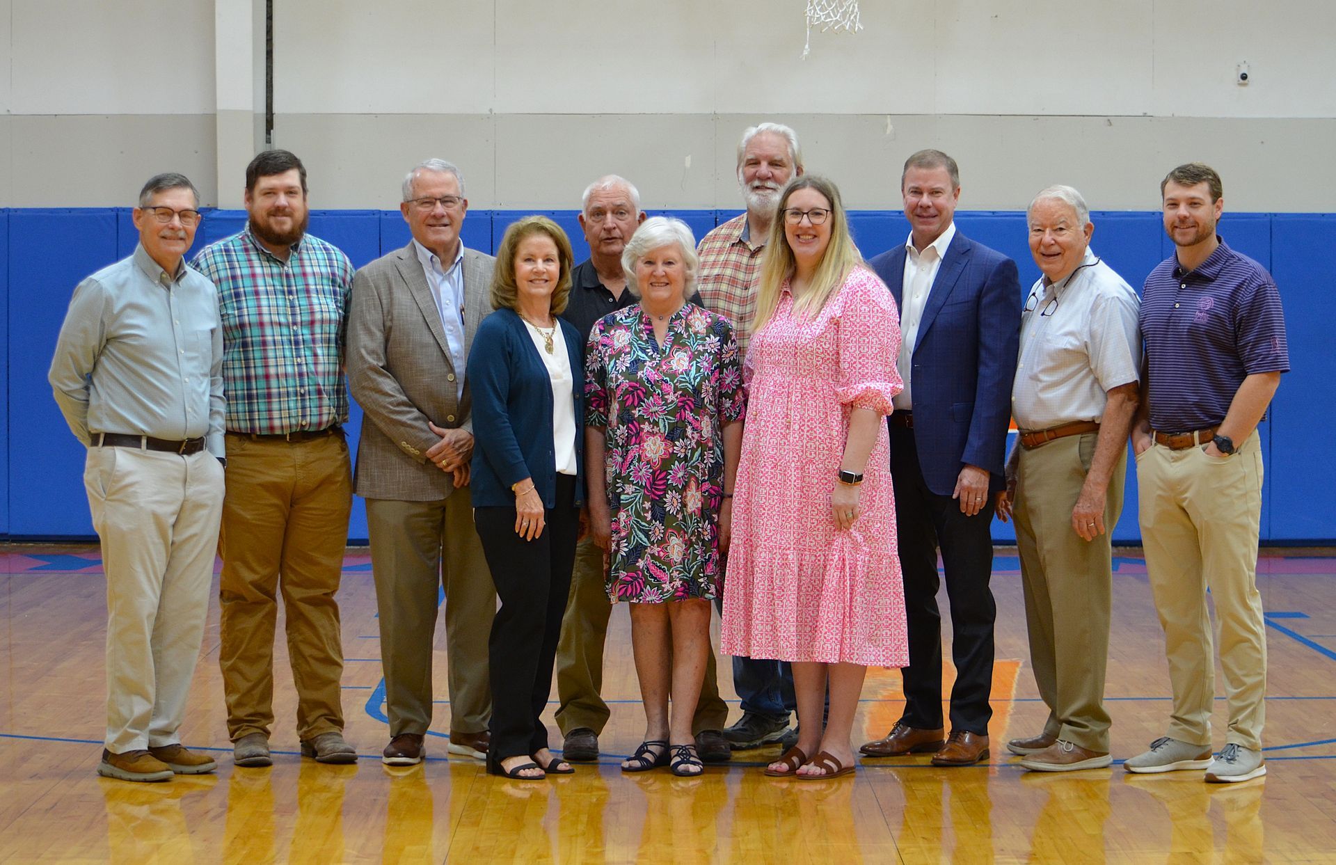Group of people posing for a photo in a gymnasium. Some are wearing suits, others casual attire.