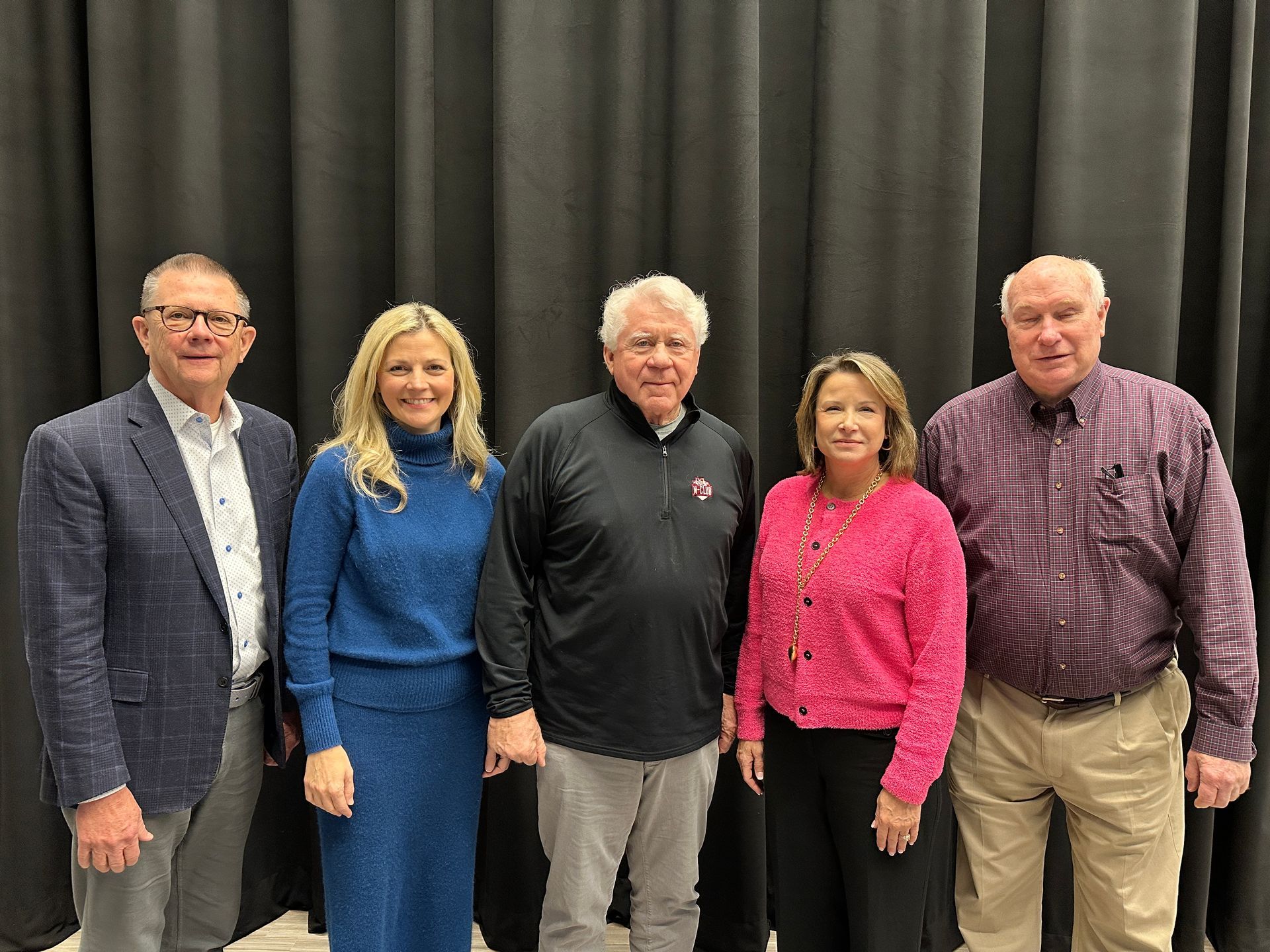 Five people standing together in front of a black backdrop. They are smiling.