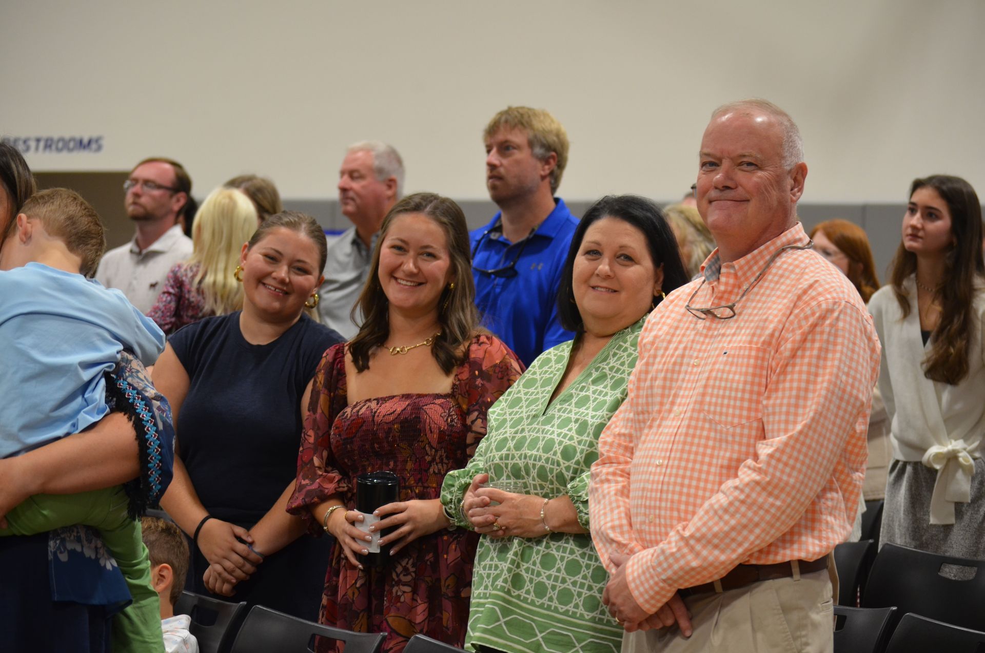 People standing inside a building. Some are smiling, many looking towards the camera.
