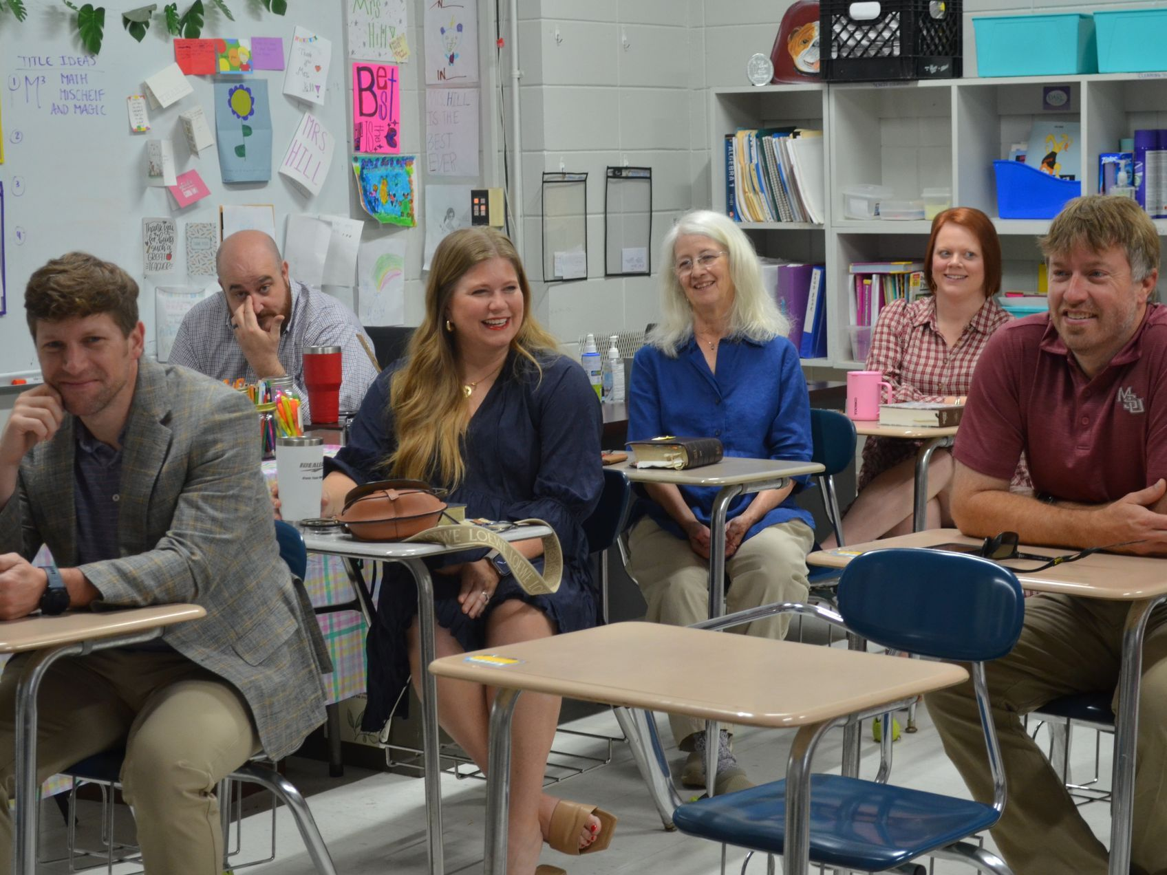A group of people are sitting at desks in a classroom.