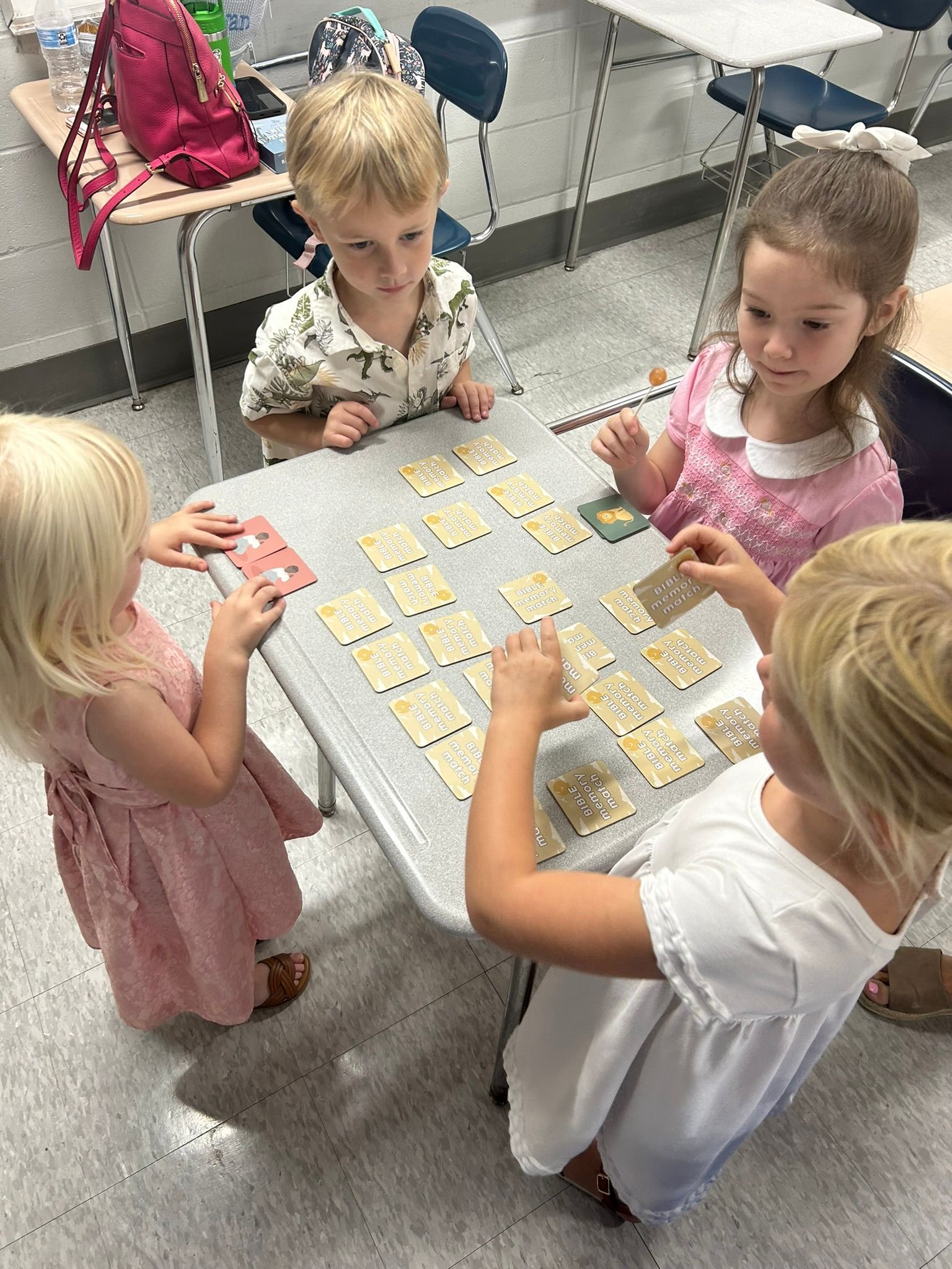 Four children playing a memory card game at a table in a classroom.