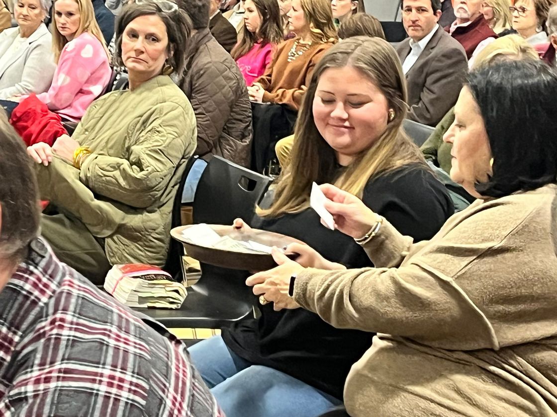People in a crowd: woman holding a plate with a raffle ticket, smiling, with another woman.