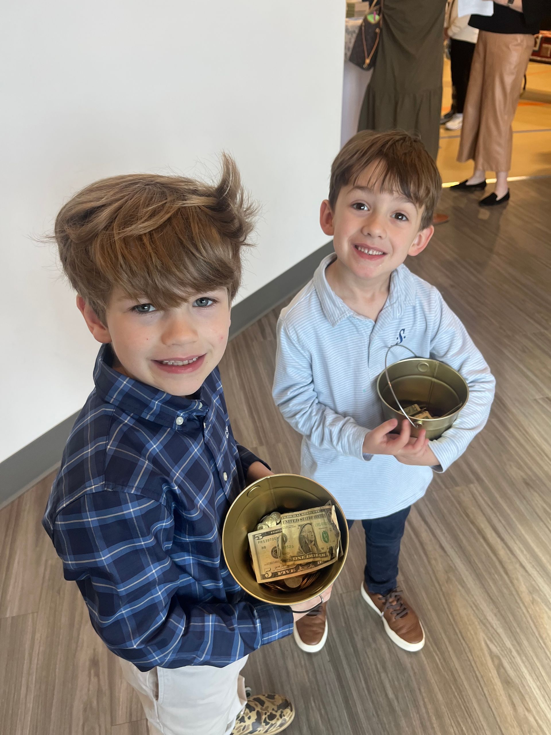 Two boys holding gold bowls with money, smiling.