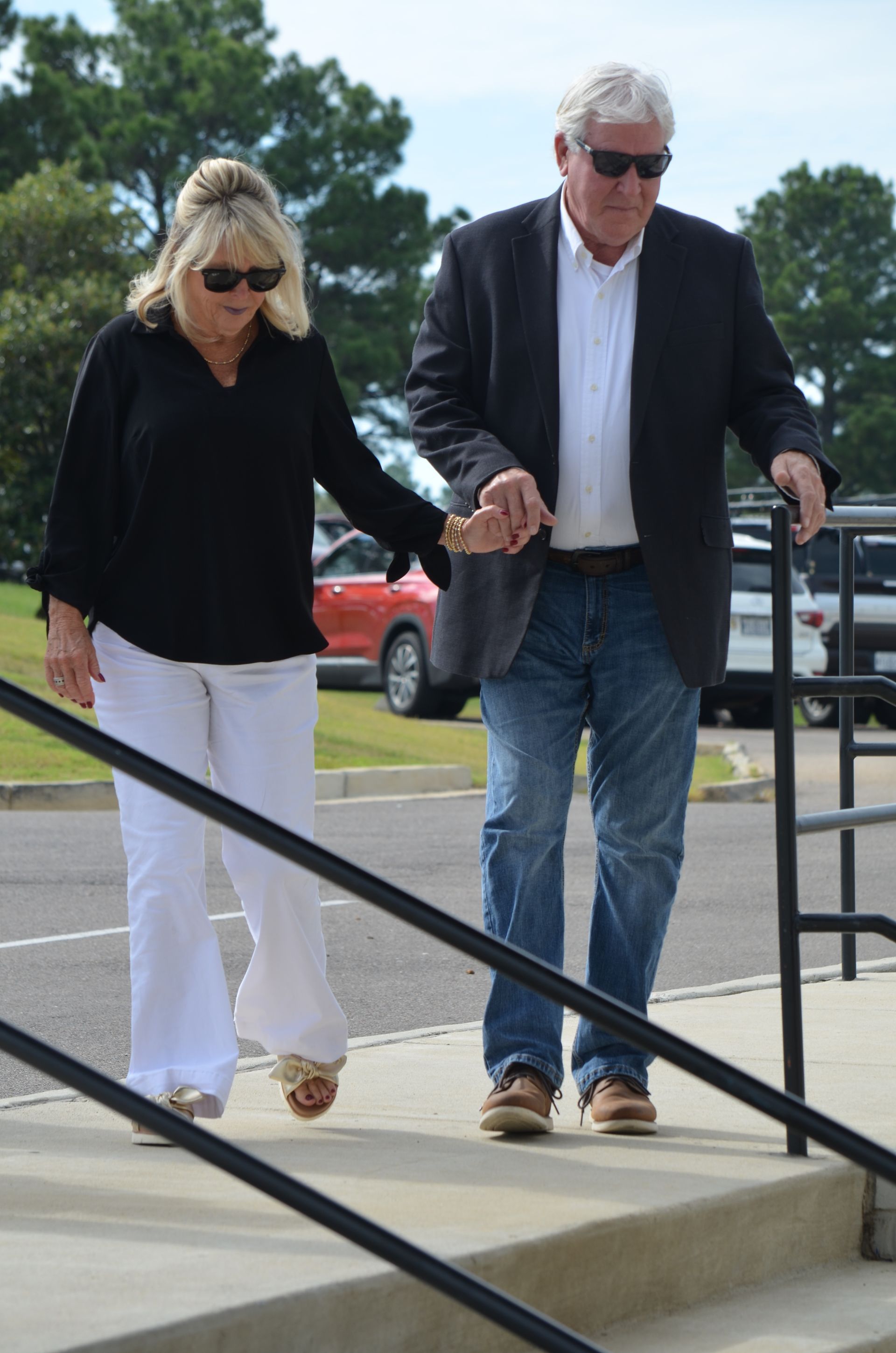 Woman in white pants and man in jeans walk down steps, holding hands.