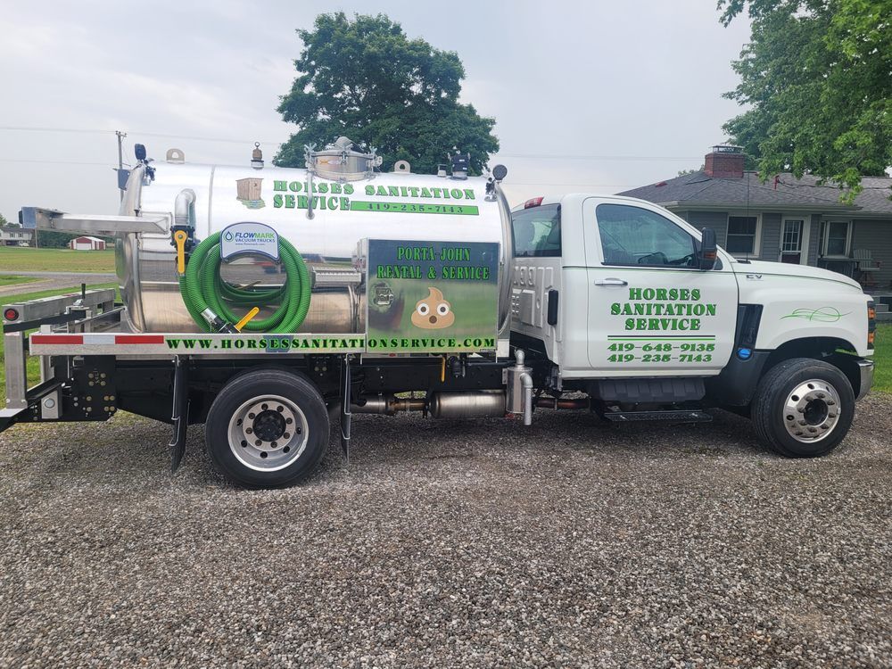 A white sanitation service truck parked on a gravel lot with green company logos and a poop emoji on the side tank.
