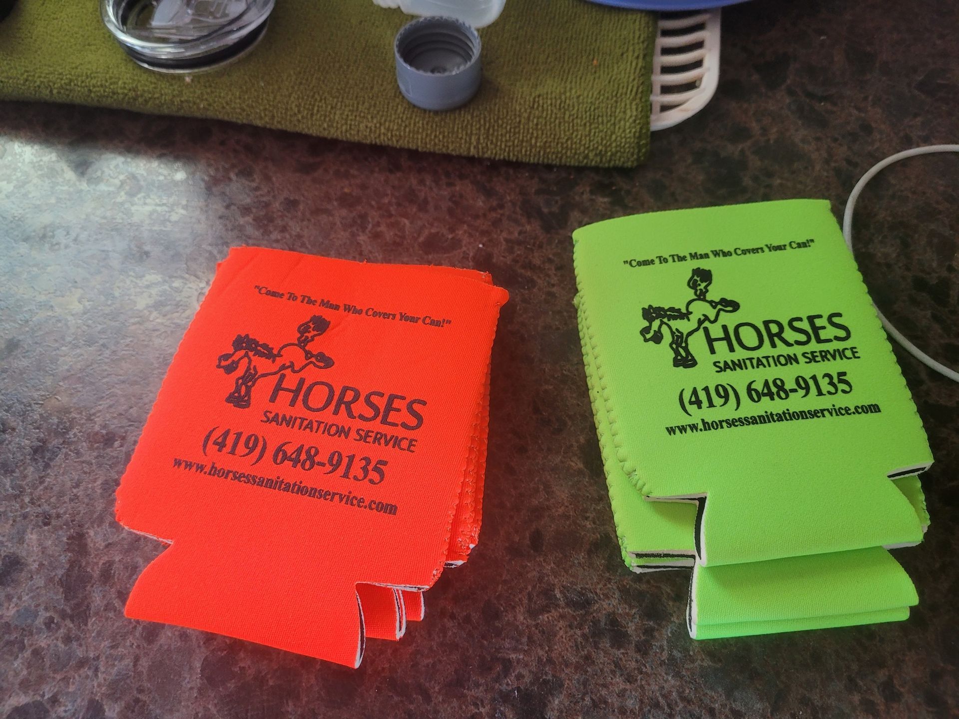 Two stacks of foam beverage coolers, one neon orange and one lime green, featuring a logo for Horses Sanitation Service.