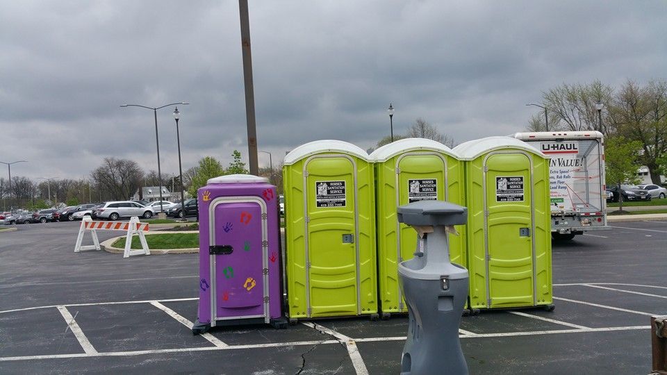 Three lime green and one purple portable toilet in an empty parking lot near a U-Haul truck.