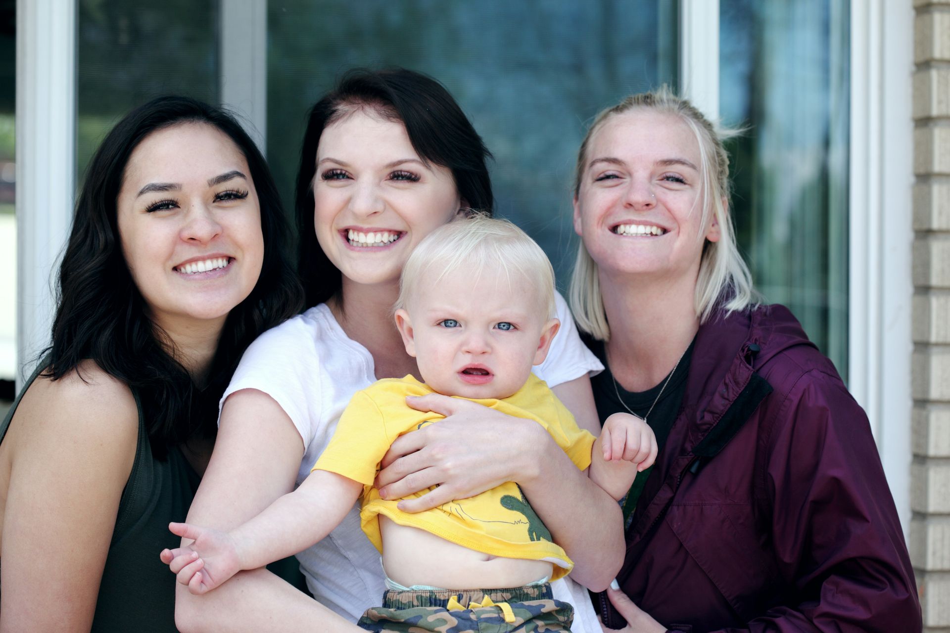 Three women are holding a baby and smiling for the camera.