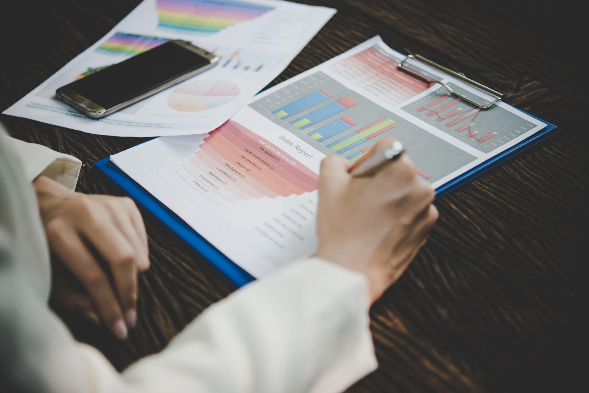 Person writing on data charts, phone nearby.