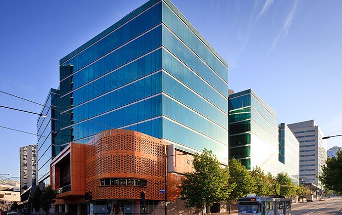 Modern glass office building with orange accent and tram passing by on a city street.