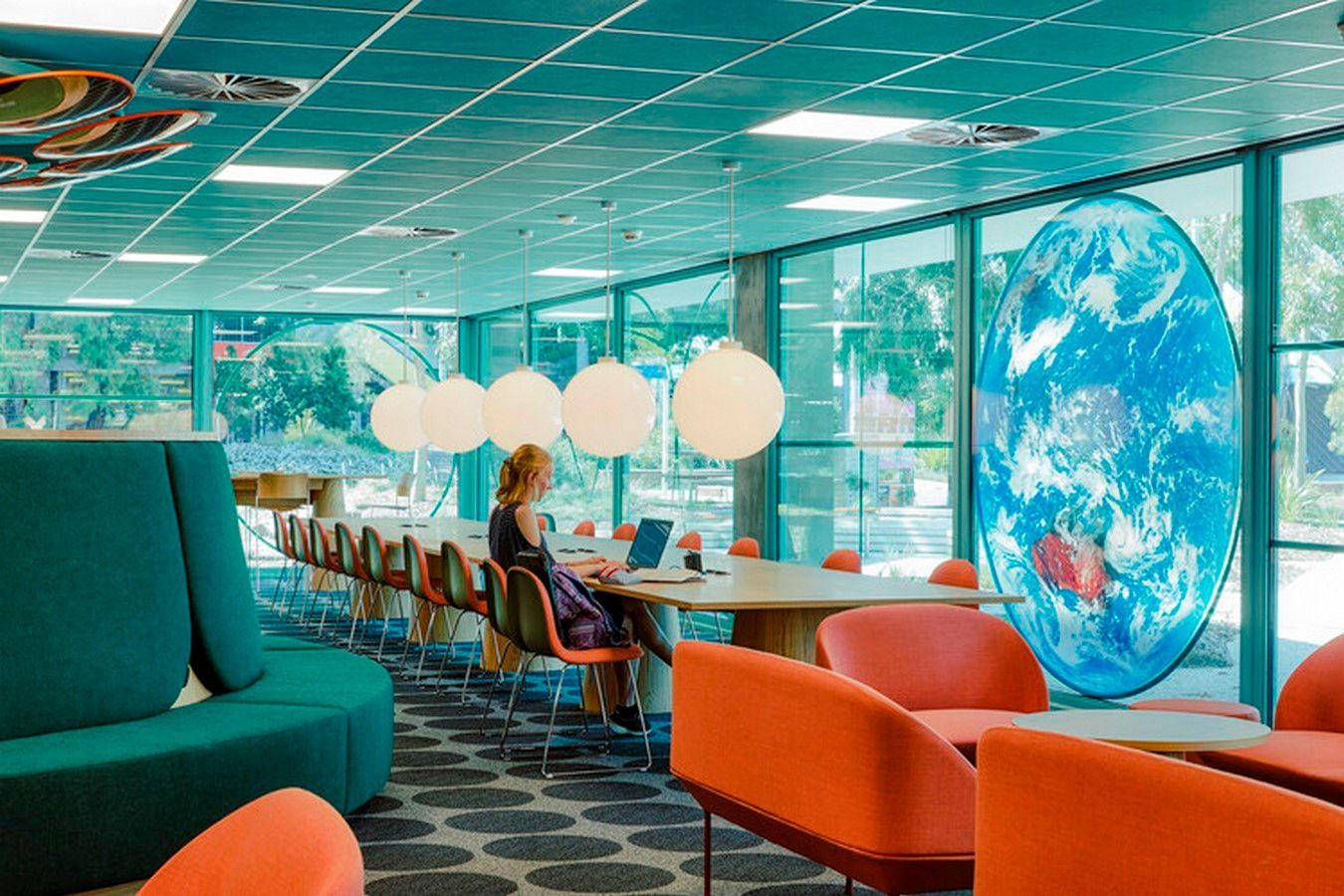 Woman working on a laptop in a colorful co-working space with an Earth graphic and globe lights.
