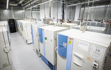 A lab with rows of white and blue refrigeration units, pipes, and wires.