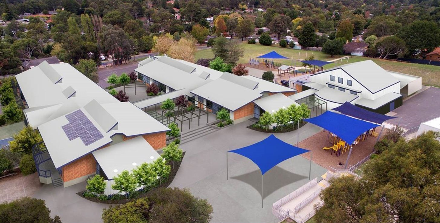 Aerial view of school campus with gray roofs, blue shade structures, and green trees.