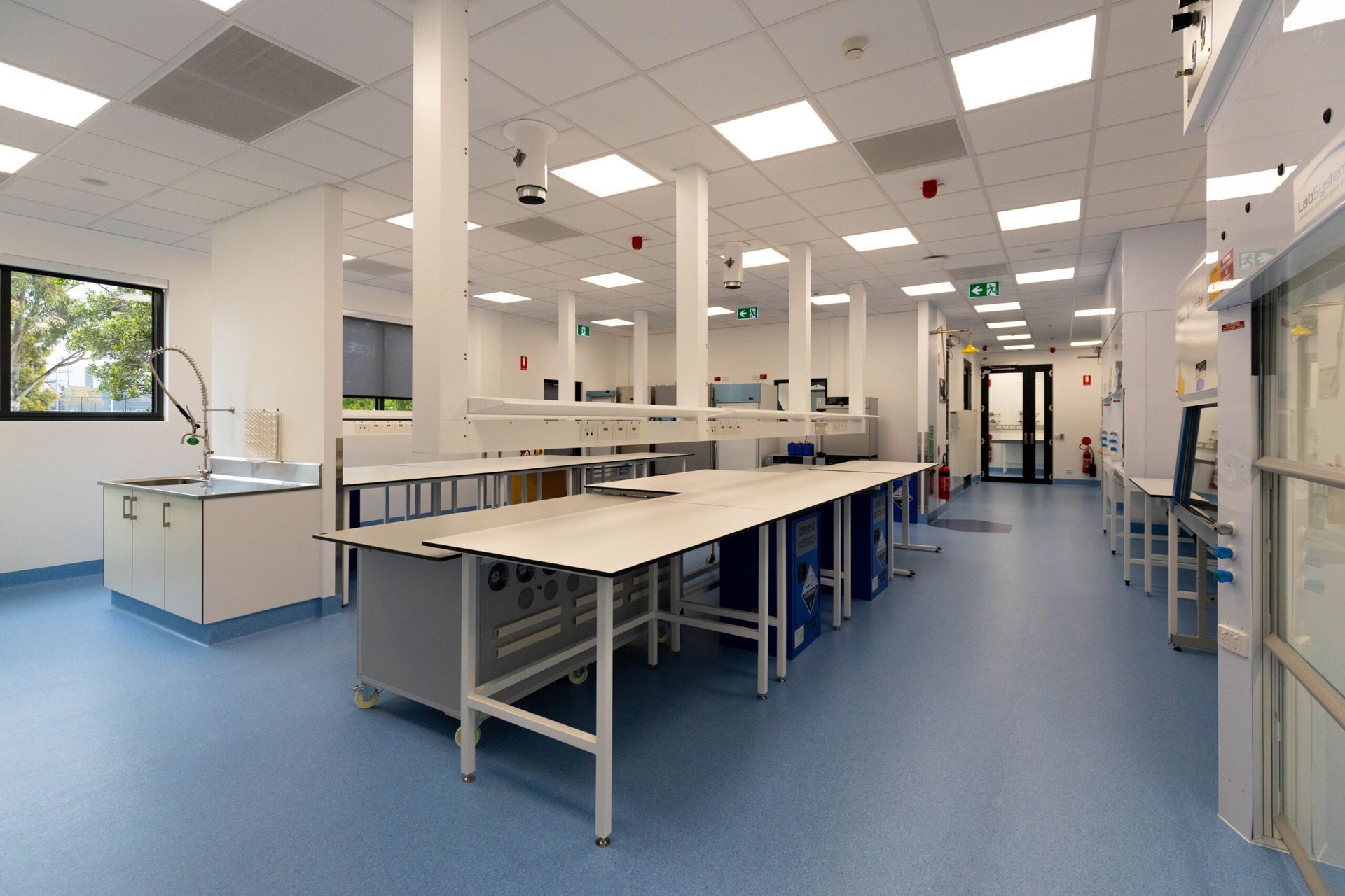 Modern laboratory interior with bright white walls, blue floor, and lab tables.