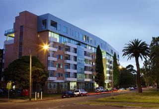 Apartment building with curved facade at dusk, cars parked on street, palm tree.