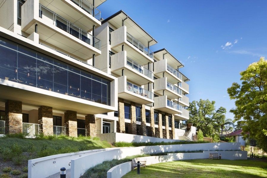Modern multi-story building with balconies, grass lawn, and blue sky.