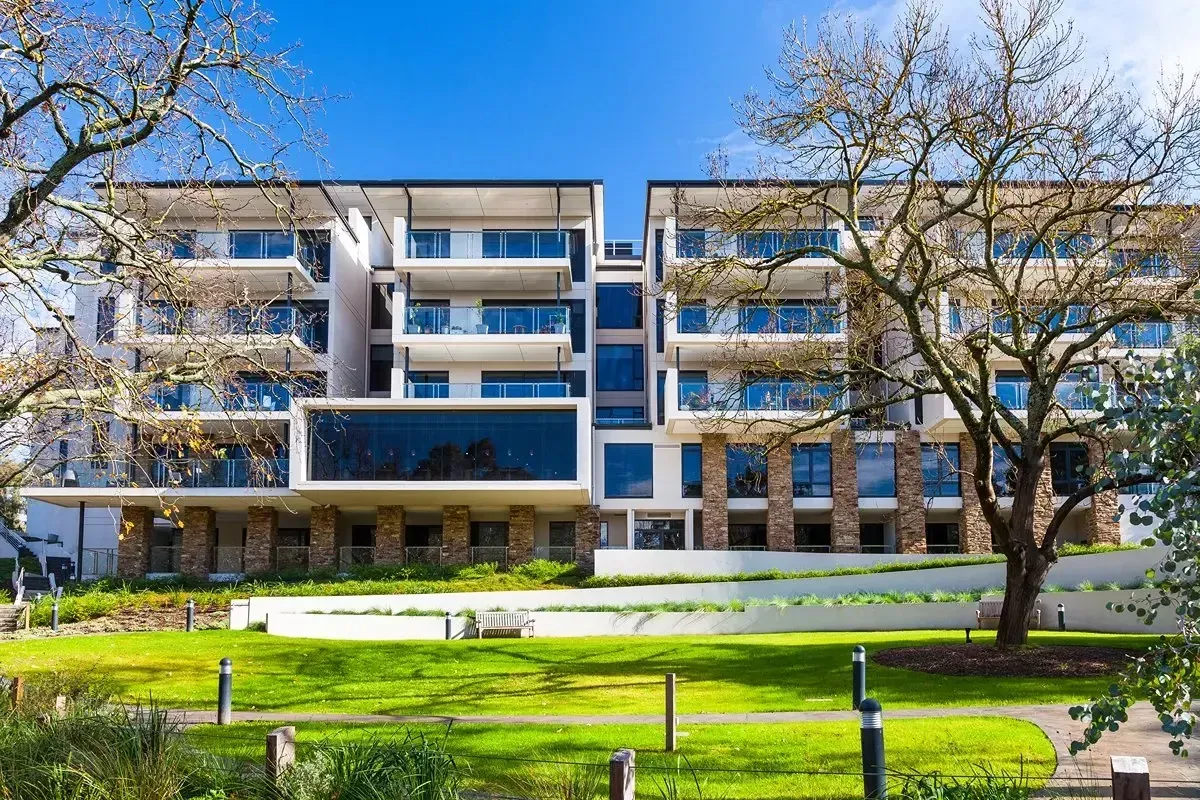 Modern multi-story building with balconies and a grassy lawn on a sunny day.