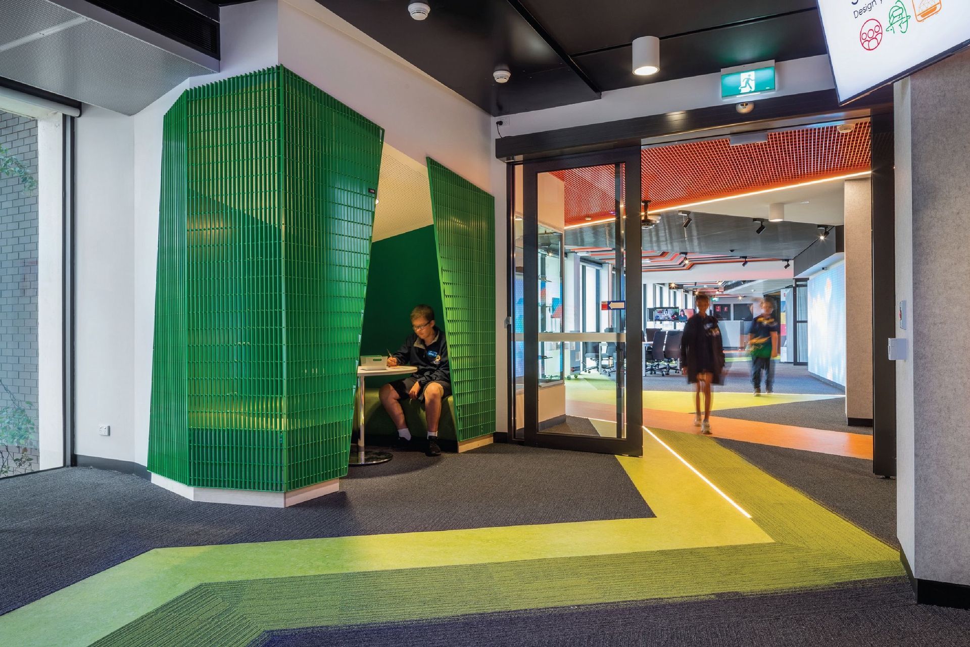 Person in a green booth, entering a modern office. Colorful floors, automatic doors.