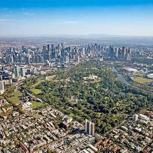 Aerial view of Melbourne, Australia, with green park in foreground and city skyline in the distance under a blue sky.