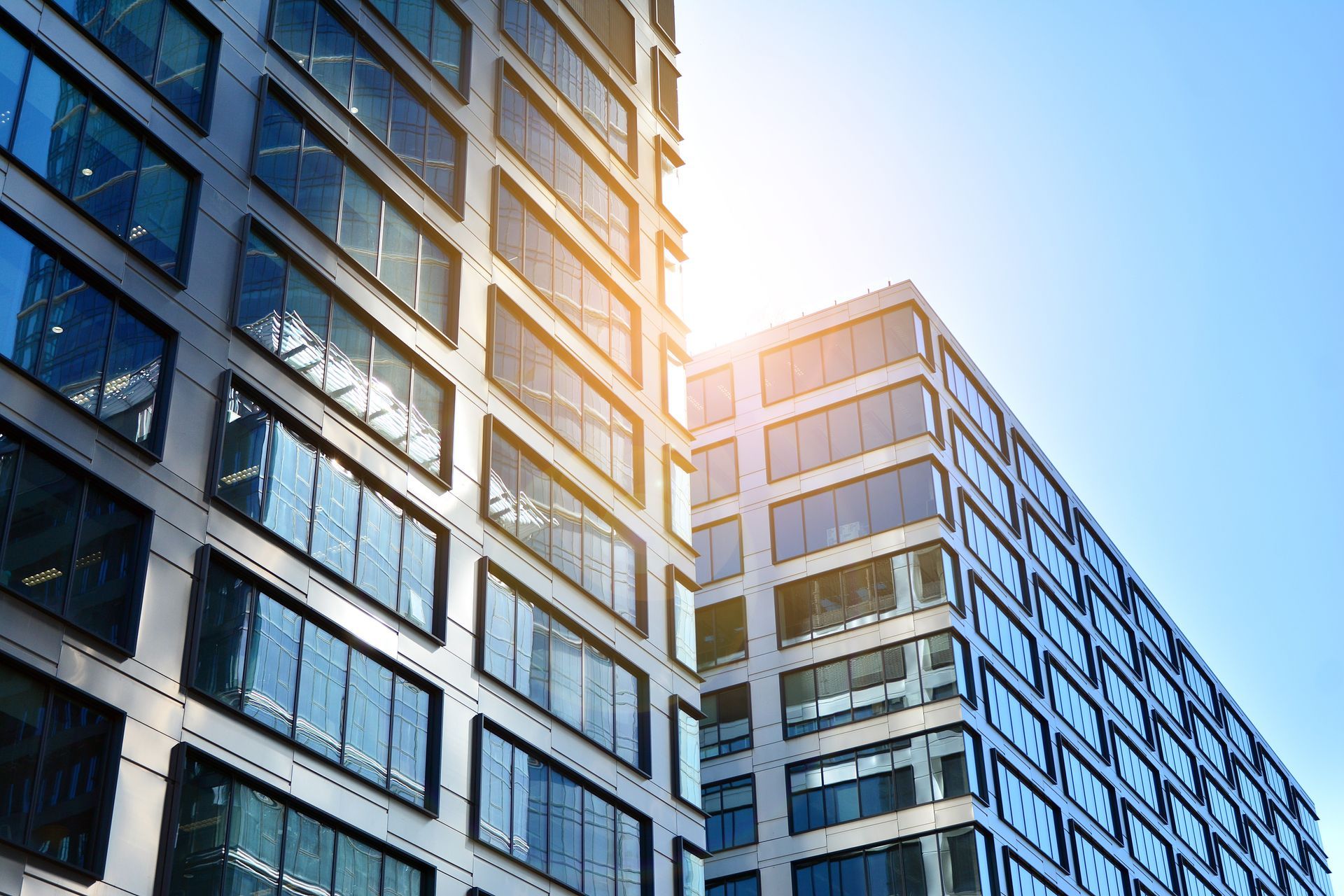 Modern glass and steel office buildings under a bright blue sky, sunlight reflecting.