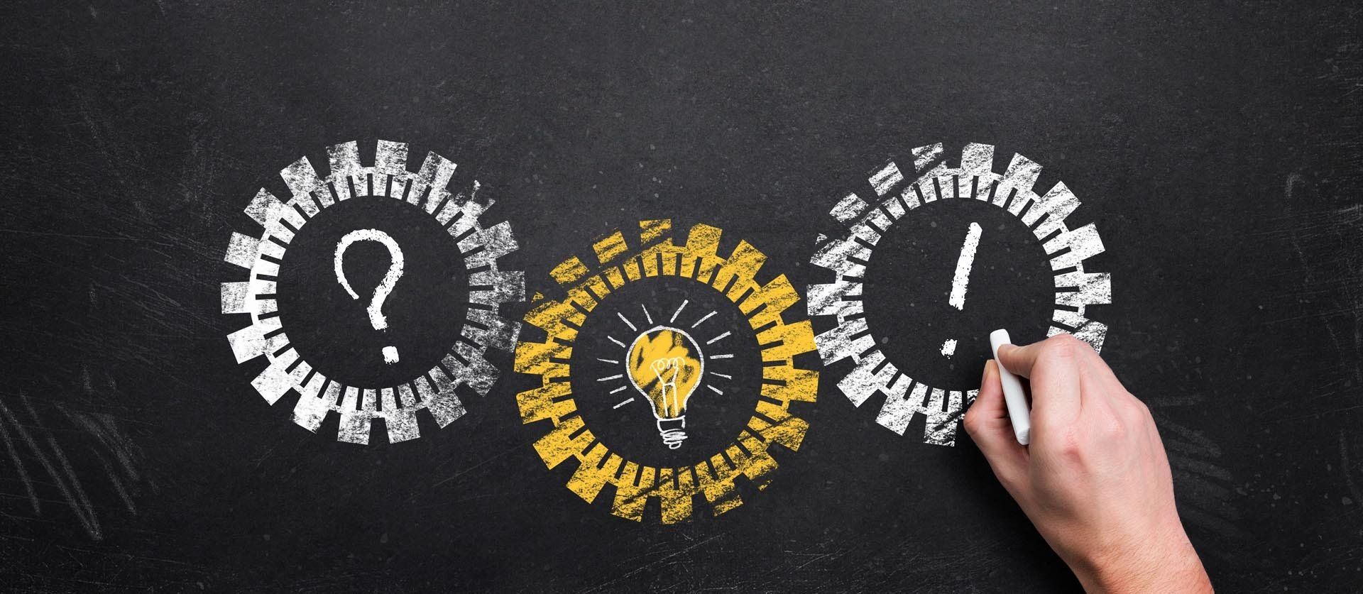 Eine Person zeichnet eine Glühbirne und ein Fragezeichen auf eine Tafel.