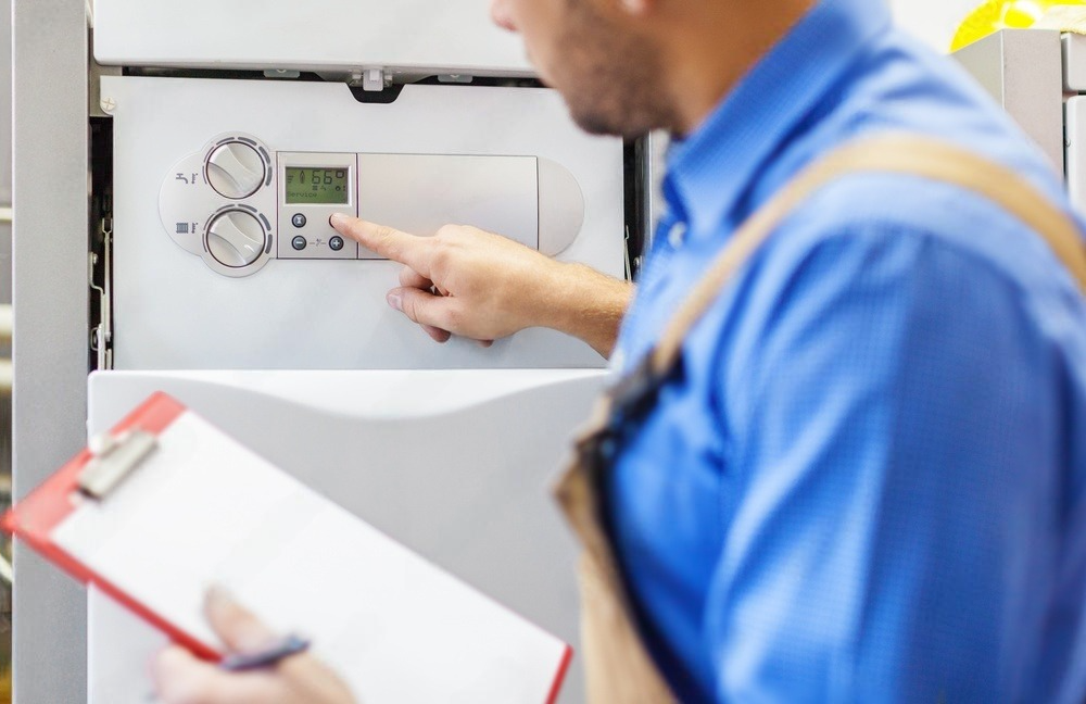 A man in a blue shirt is holding a clipboard in front of a heater.