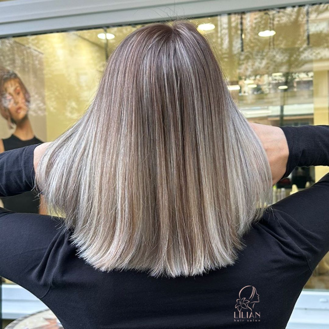 Eine Frau mit langen Haaren steht mit verschränkten Armen vor einem Fenster.