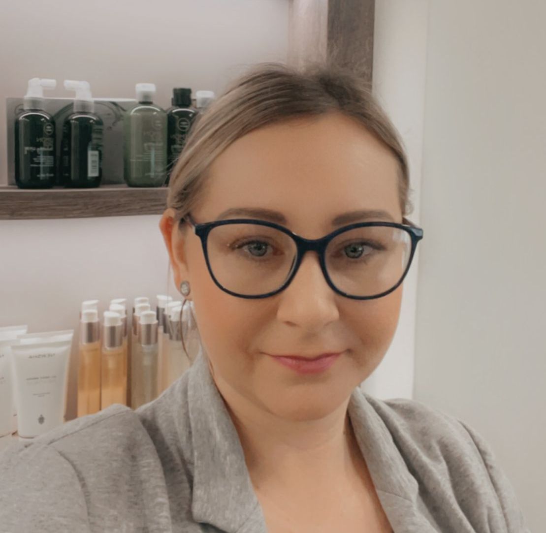 Eine Frau mit Brille lächelt vor einem Regal voller Flaschen