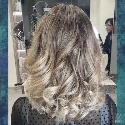 Eine Frau mit langen blonden Haaren steht in einem Salon vor einem Spiegel.