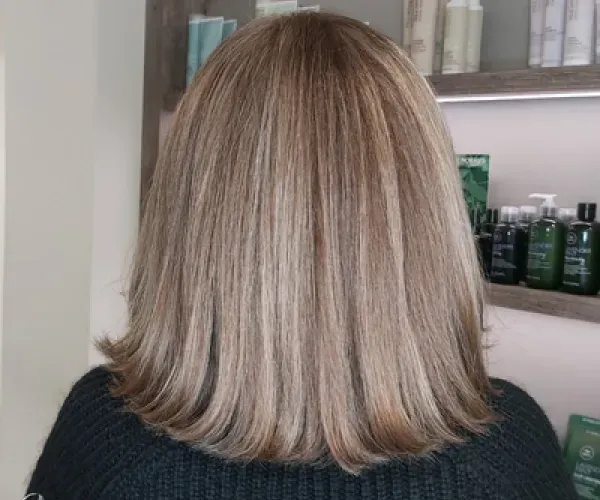 Eine Frau mit langen blonden Haaren steht vor einem Regal mit Flaschen voller Haarpflegeprodukte.