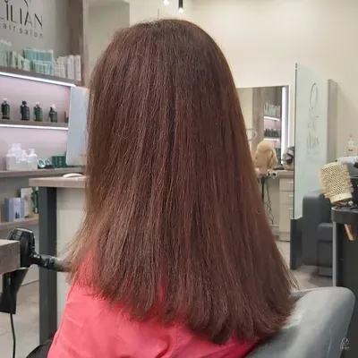 Eine Frau mit langen braunen Haaren sitzt auf einem Stuhl in einem Salon