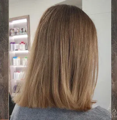 Eine Frau mit langen Haaren sitzt in einem Salon vor einem Spiegel.