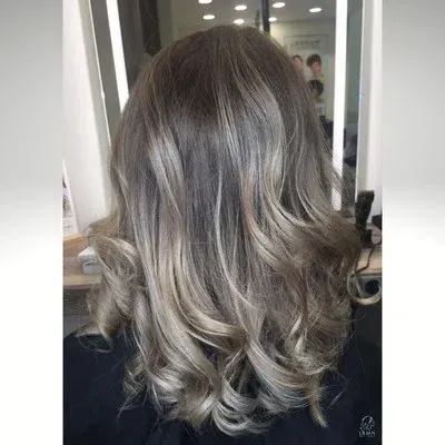 Eine Frau mit grauem Haar steht in einem Salon vor einem Spiegel.