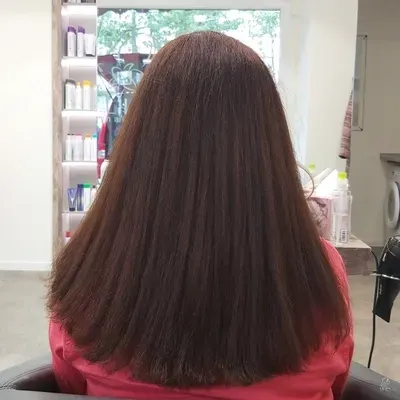 Eine Frau mit langen braunen Haaren sitzt auf einem Stuhl in einem Salon.