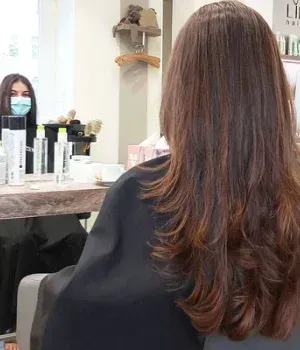 Eine Frau mit langen Haaren sitzt in einem Friseursalon auf einem Stuhl.