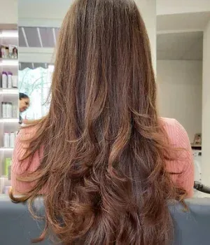 Eine Frau mit langen braunen Haaren sitzt auf einem Stuhl in einem Salon.