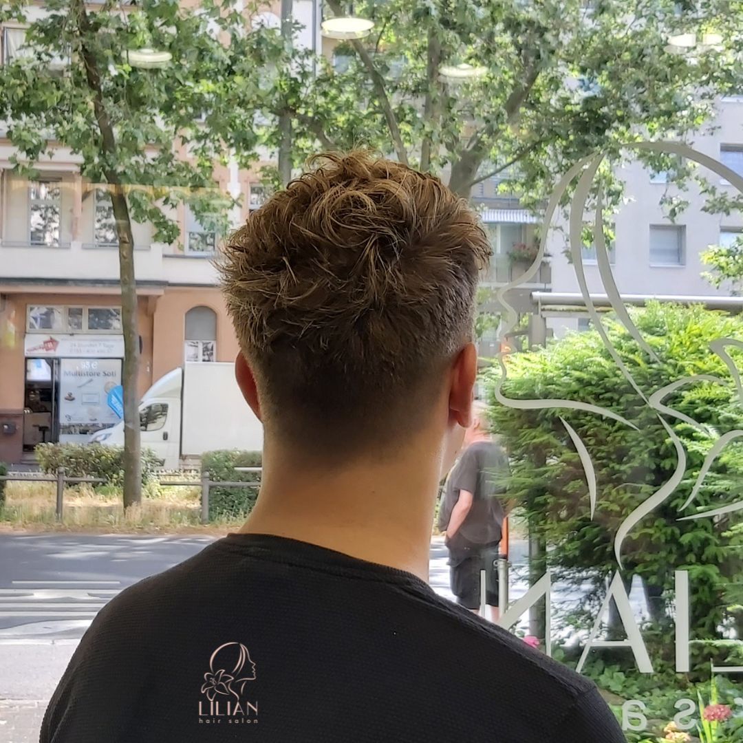 Ein Mann mit lockigem Haar steht vor einem Fenster.