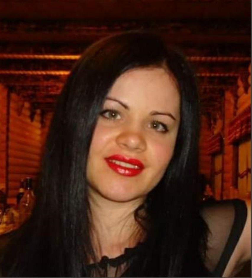 Eine Frau mit langen schwarzen Haaren und rotem Lippenstift lächelt in die Kamera