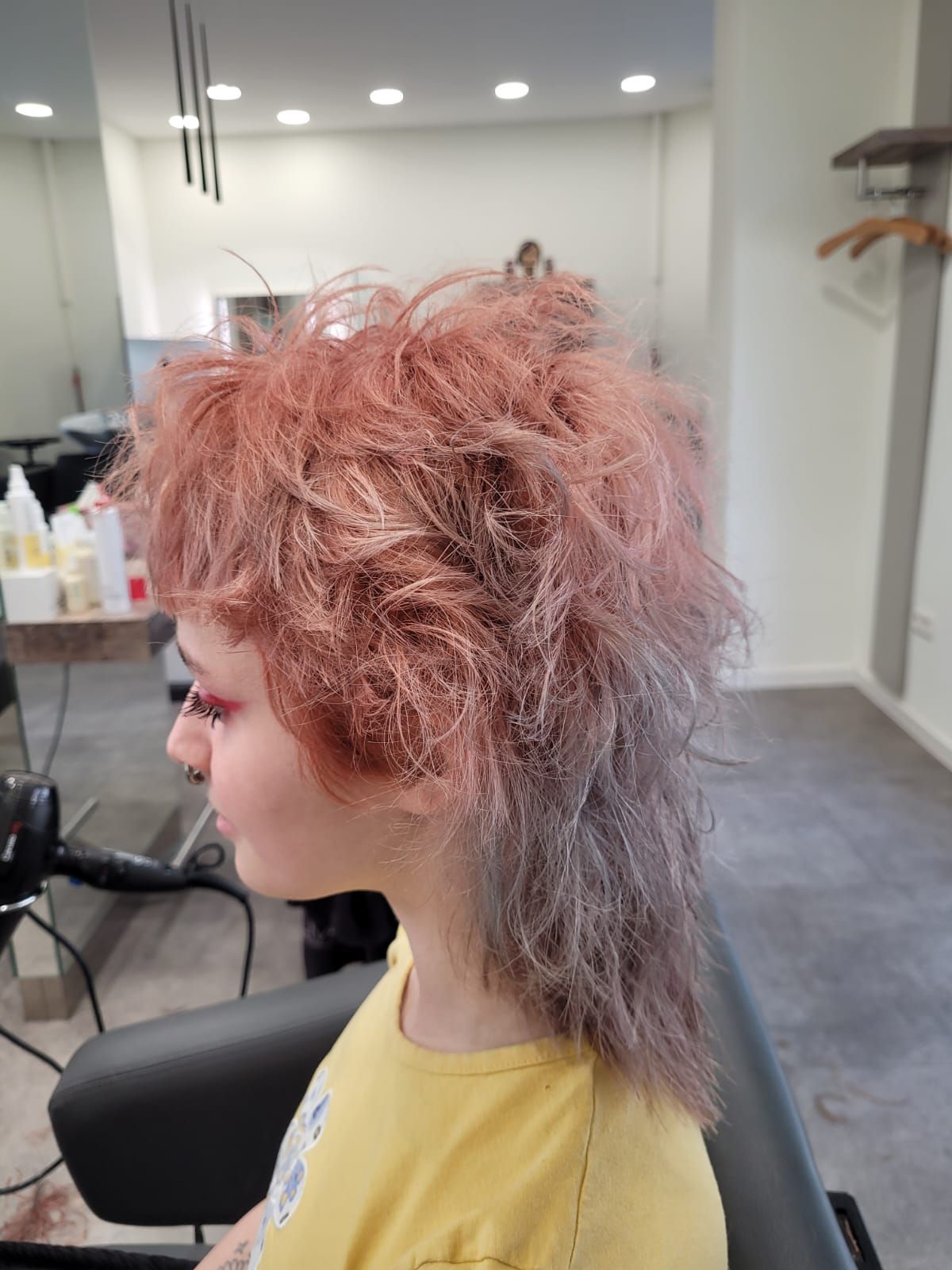 Eine Frau mit rosa Haaren sitzt in einem Salon auf einem Stuhl.
