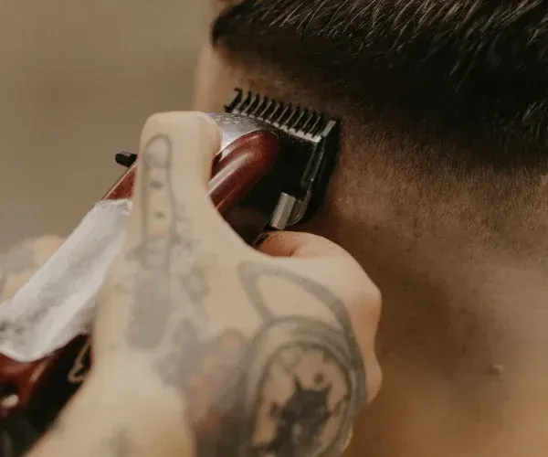 Ein Mann mit einer Tätowierung auf dem Arm lässt sich von einem Friseur die Haare schneiden.