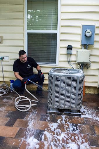 A man is cleaning an air conditioner outside of a house.