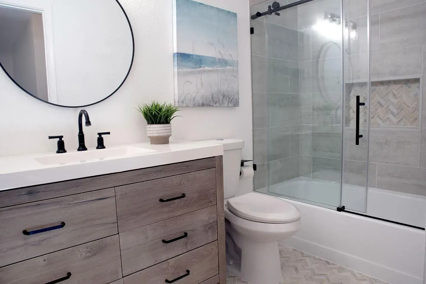 Bathroom with gray vanity, black fixtures, round mirror, and a glass shower door.