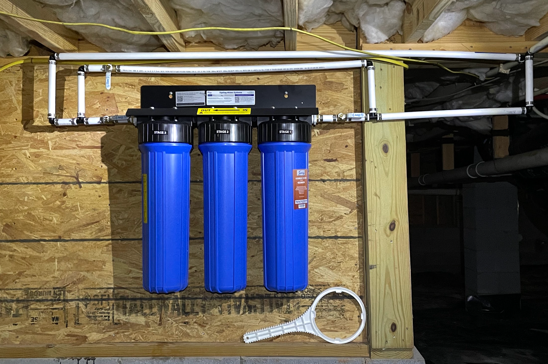 Water filtration system with three blue filter housings, installed on a wooden wall.