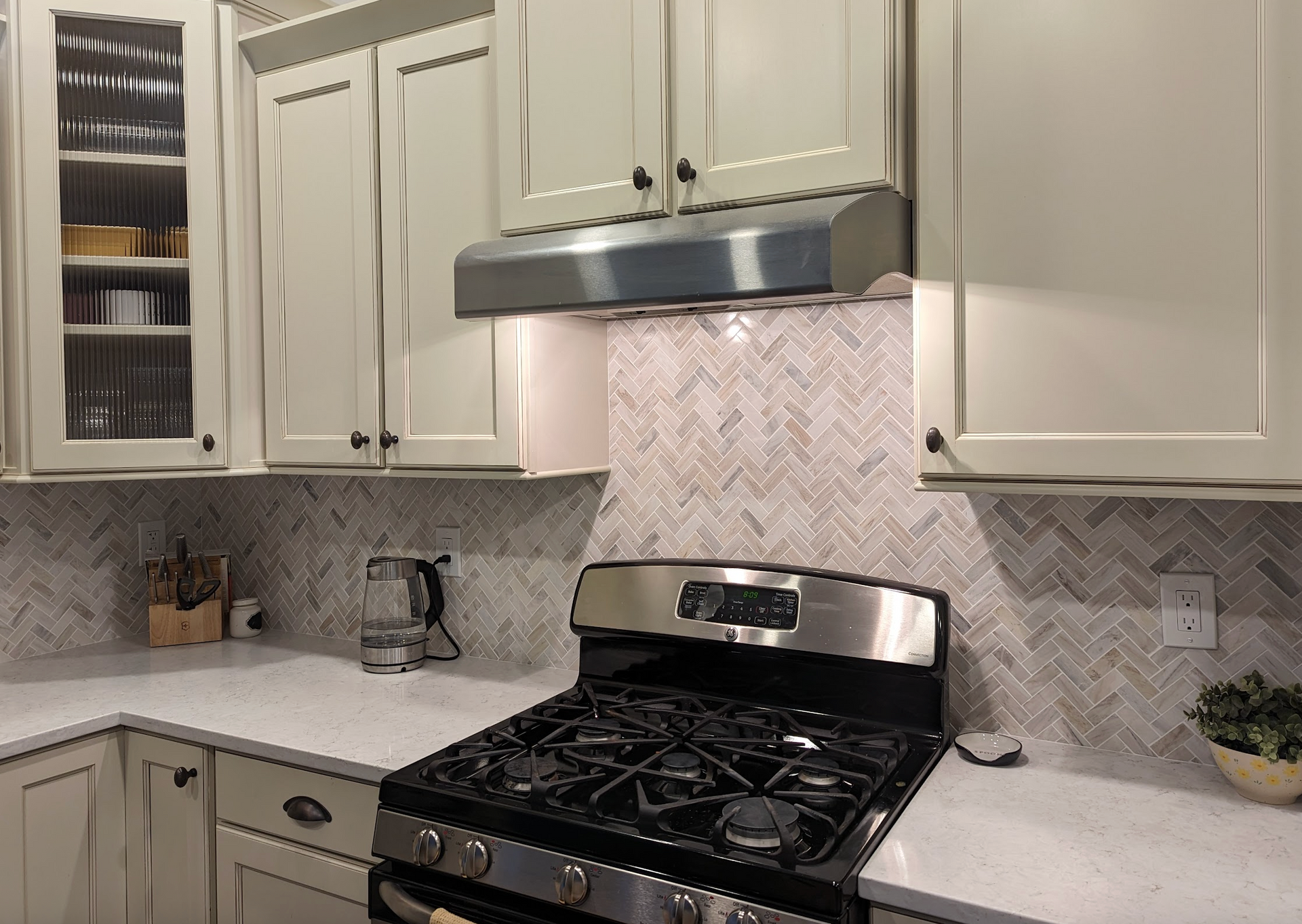 Kitchen with light green cabinets, stainless steel appliances, and herringbone backsplash.