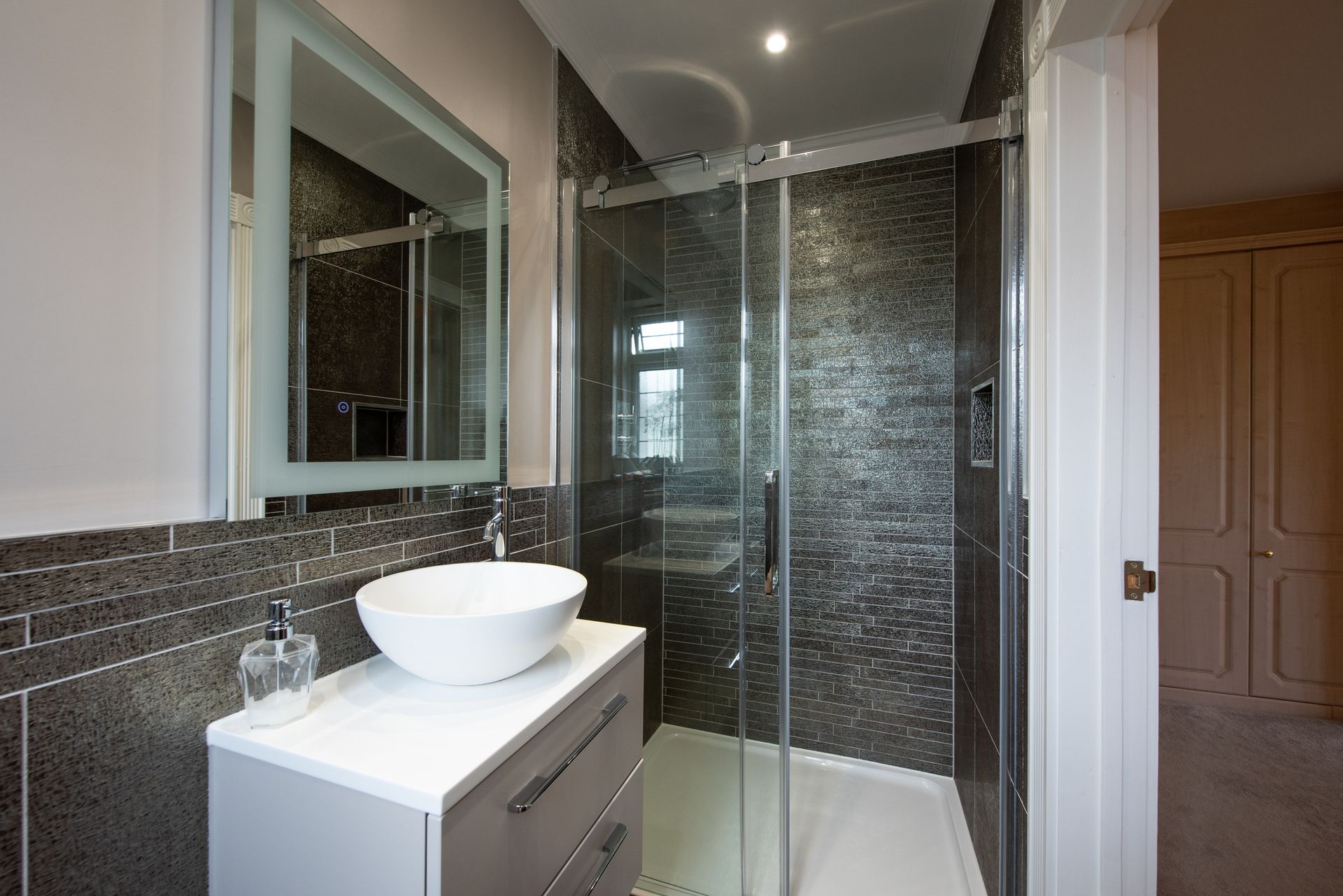 A general interior view of a small grey and white en-suite bathroom with round sink