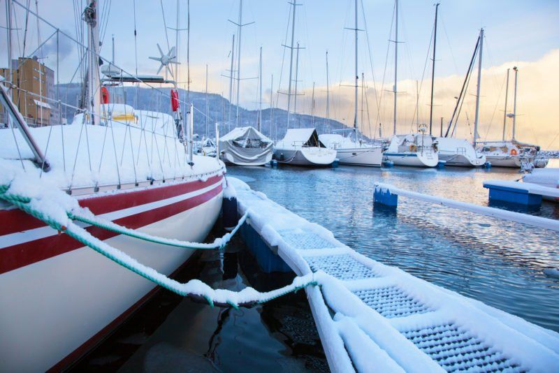 A group of boats are docked in a harbor covered in snow.
