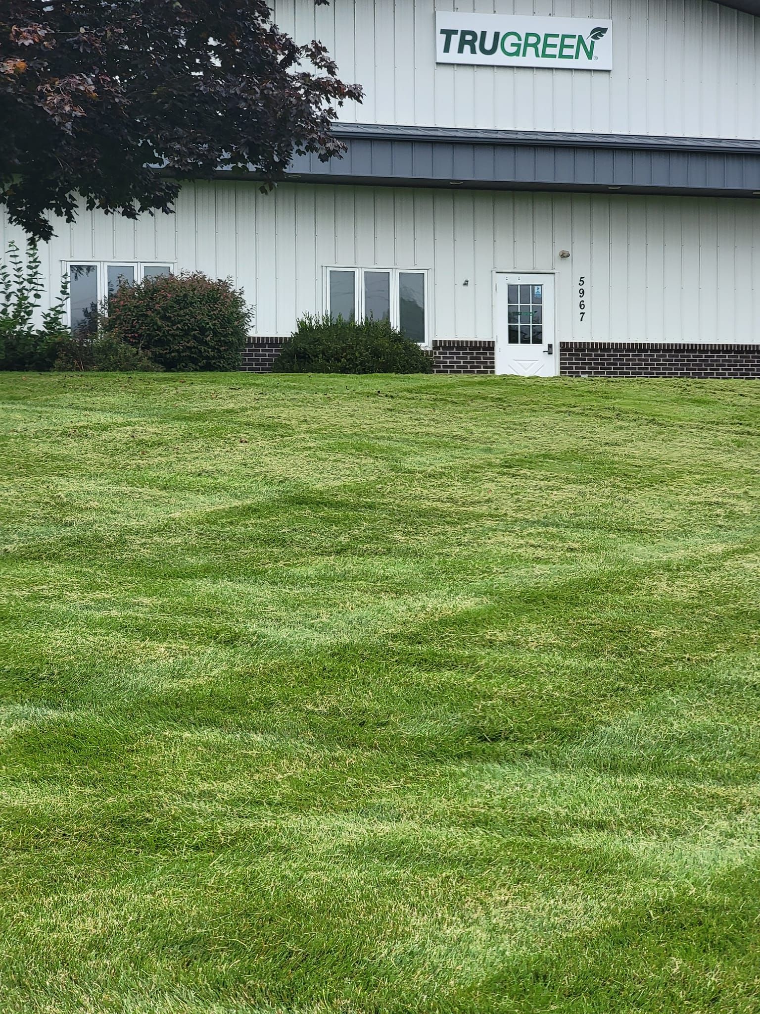 A TruGreen facility building with white metal siding and a patch of grass showing distinct lawn mowing patterns in the front.